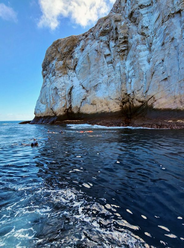 a boat traveling past a large rock formation in the ocean